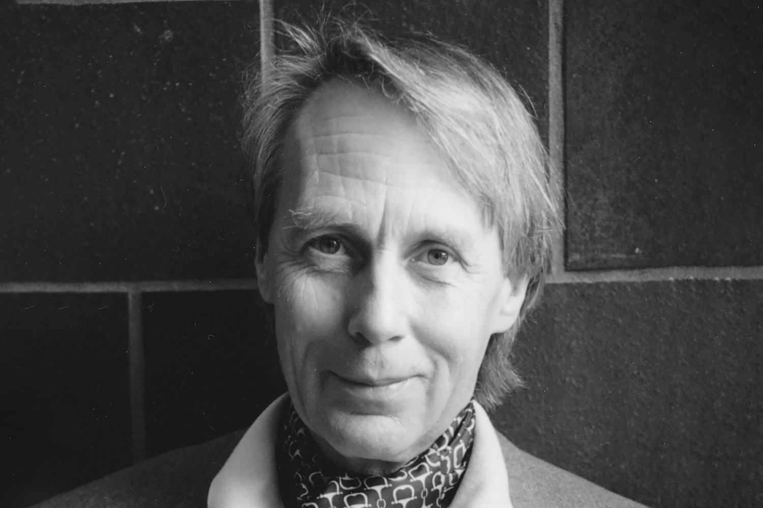 Close-up portrait of Antony Jameson standing before a tiled wall.