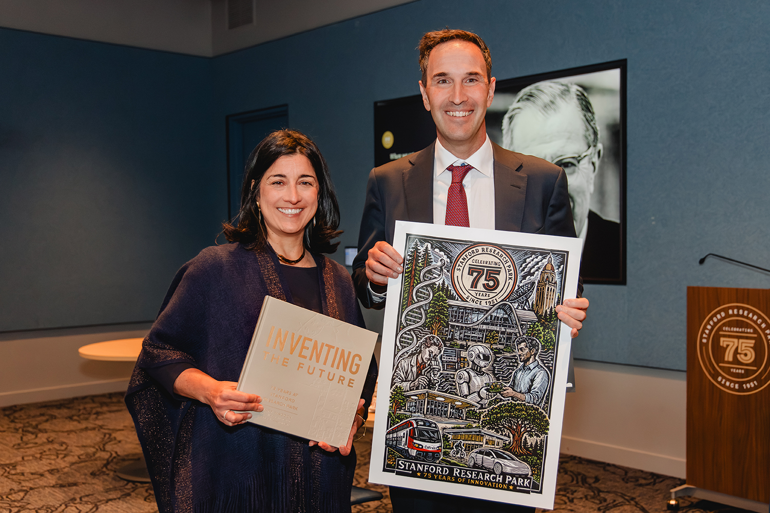 Tiffany Griego and Jonathan Levin, holding the book “Inventing the Future” and an illustrated Stanford Research Park 75th-anniversary poster.