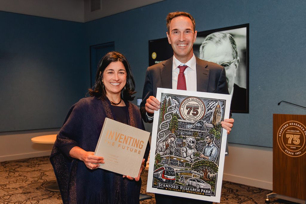 Tiffany Griego and Jonathan Levin, holding the book “Inventing the Future” and an illustrated Stanford Research Park 75th-anniversary poster.