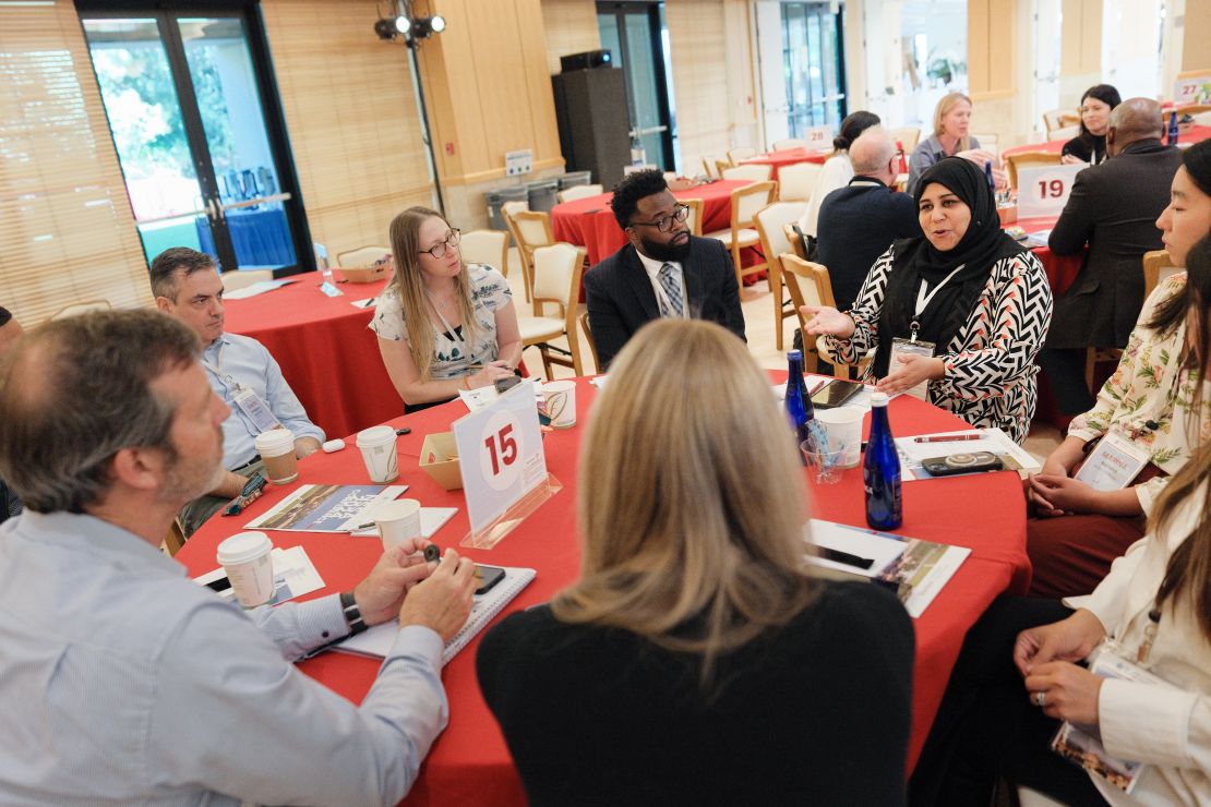 Seven adults sit around a conference table, having a conversation.