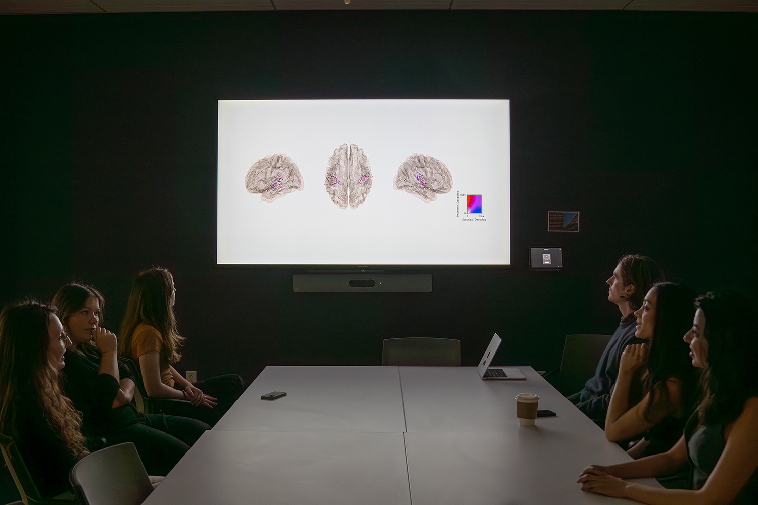 A conference room displays brain imaging on a screen while attendees engage in discussion.