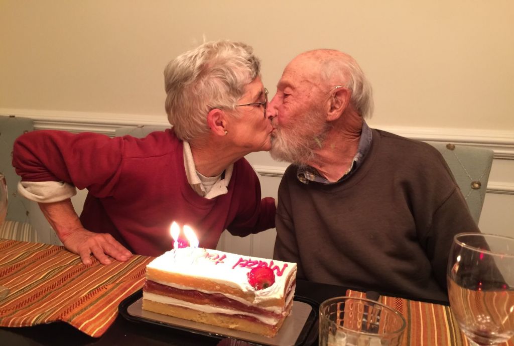 Alice Whittemore and Joseph Keller lean in for a kiss. A cake on the table before them is decorated with candles and the words Mazel Tov.