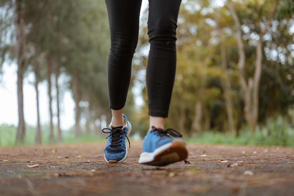 A person jogs along a tree-lined path wearing blue running shoes and black leggings.