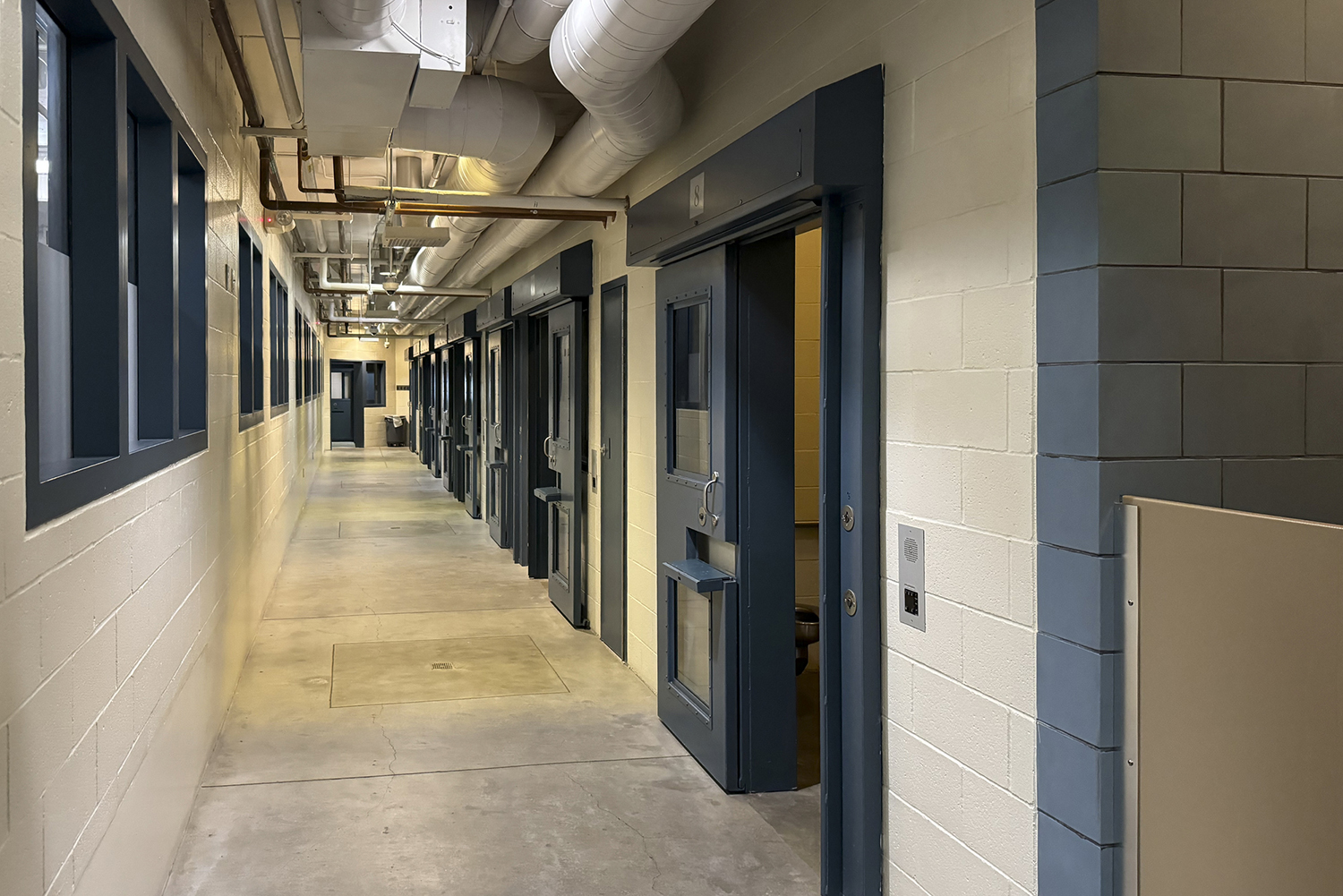 A narrow corridor with doors on one side, leading to small rooms in a prison.