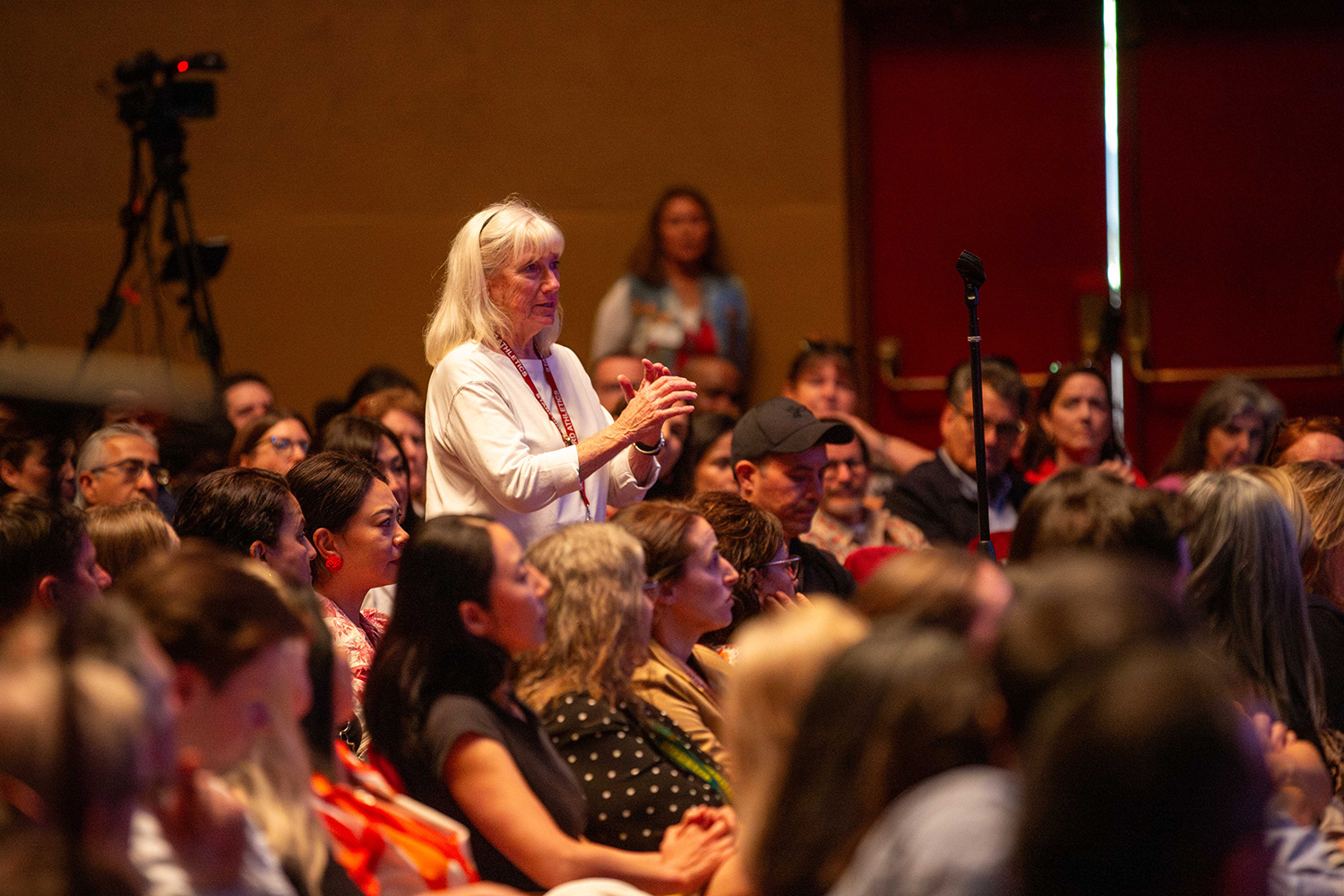 Cathy Haas standing and gesturing during a Q&A, while the audience around her watches the stage.