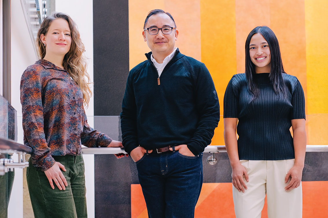 Emily Robitschek, Daniel Ho, and Ally Casasola stand together with a colorful wall mural behind them.