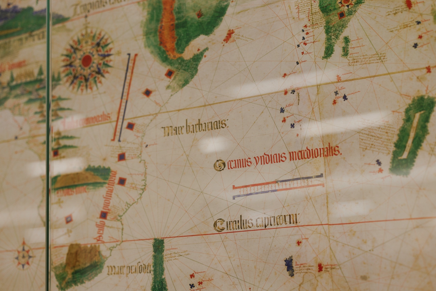 An ancient map features decorative illustrations, including seas and regions labeled in red and green text, showcasing maritime exploration.