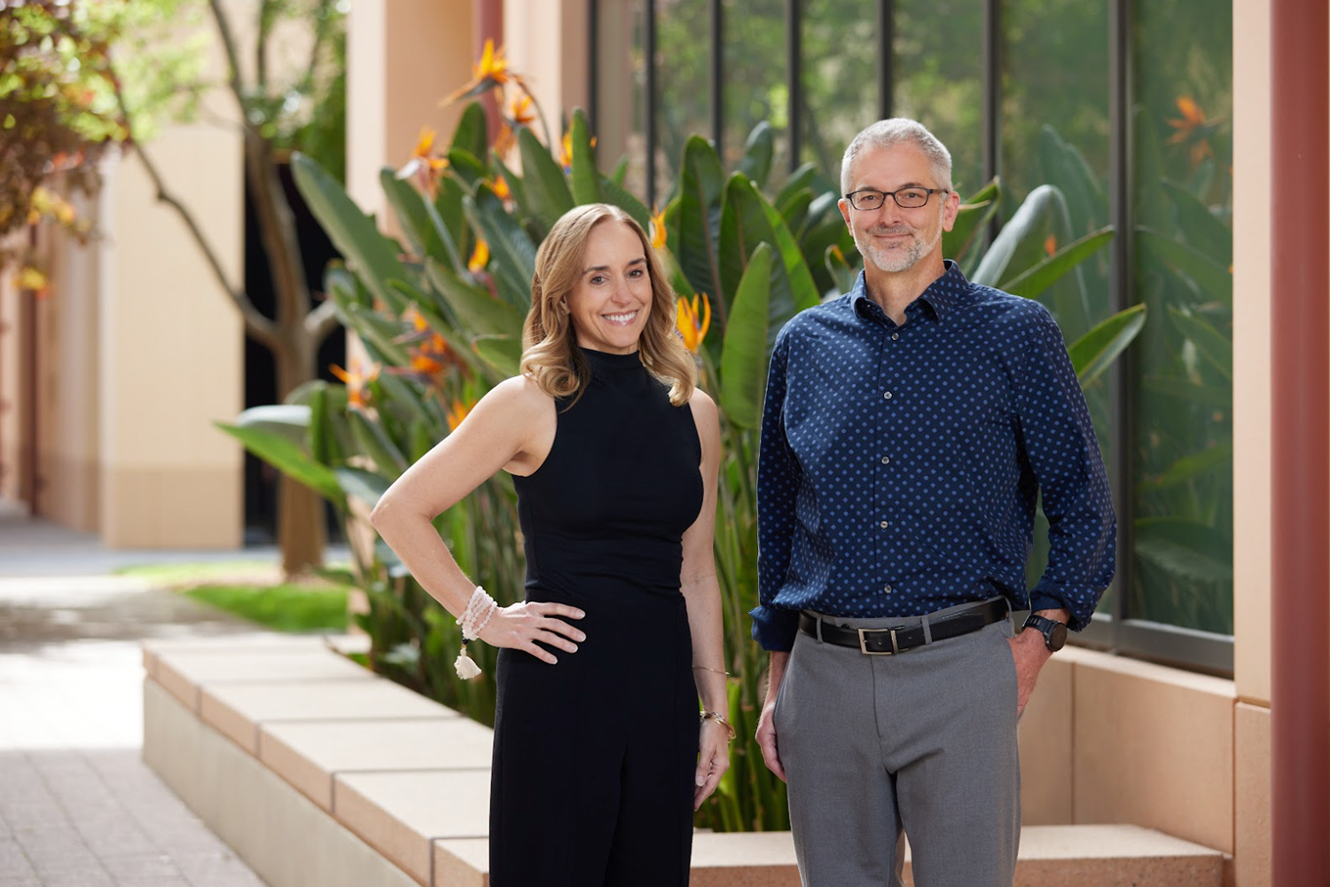 Maria Frantz and Ken Shotts stand outdoors near tropical plants, posing confidently for a photograph.