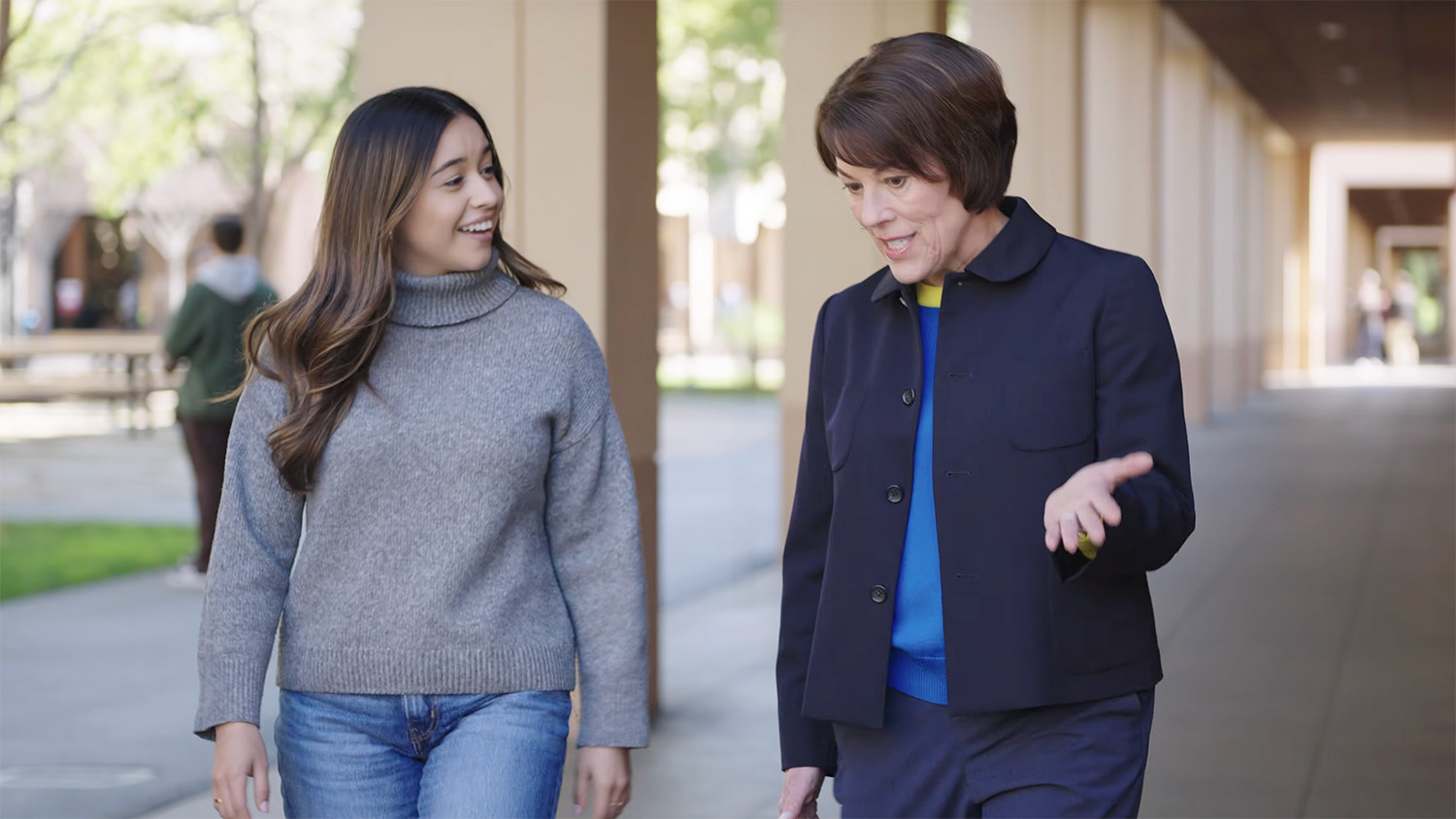 Two women walk and talk together along a pathway in an outdoor setting on the Stanford campus.