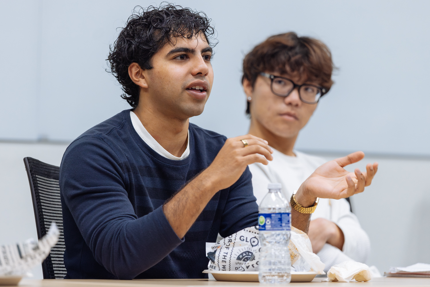 Two individuals engaged in conversation at a table with food and drinks, in a casual meeting setting.