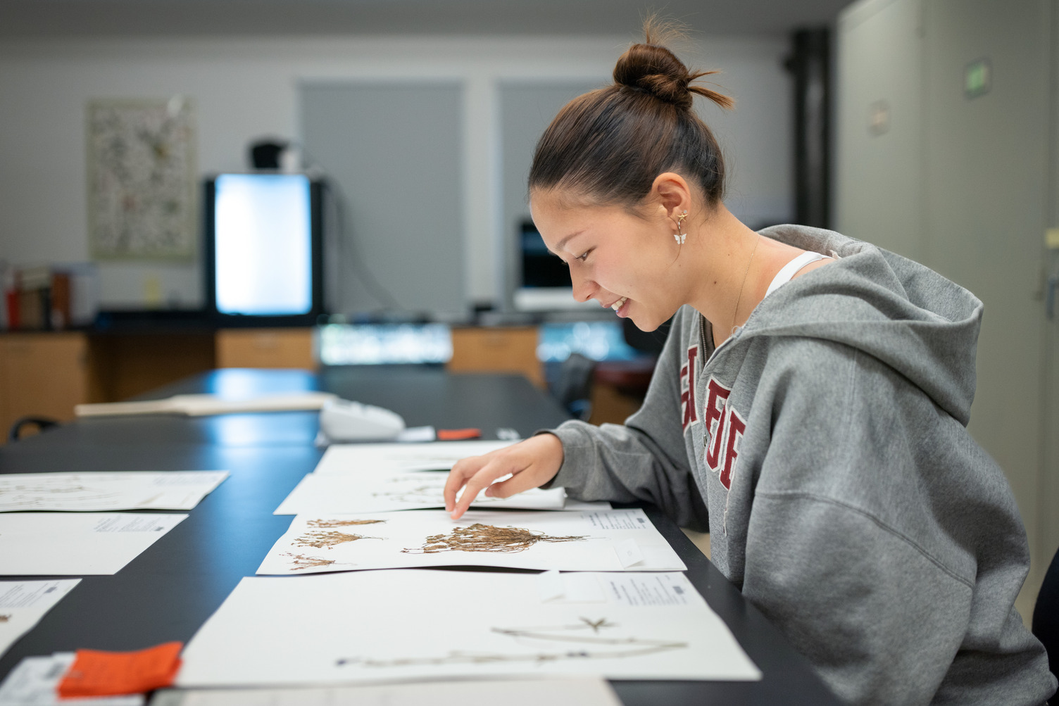 A student studies botanical specimens on a table in a research setting.