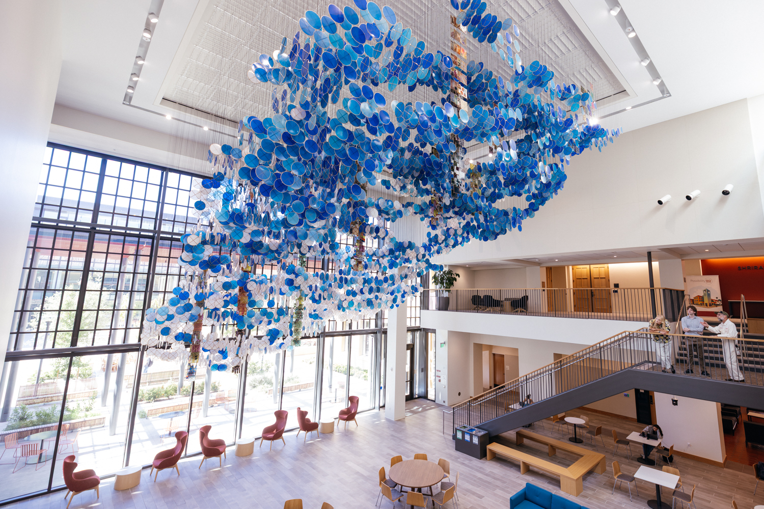 Suspended sculpture of thousands of blue and white discs fills the sunlit atrium of a Graduate School of Education building.