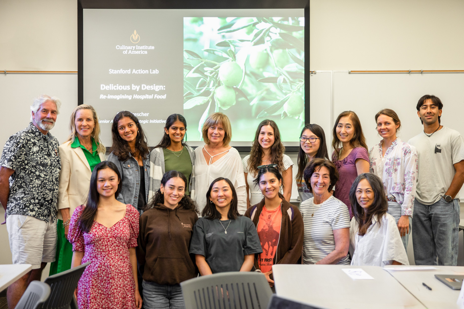 Group of students and faculty pose in a classroom before a slide reading 
