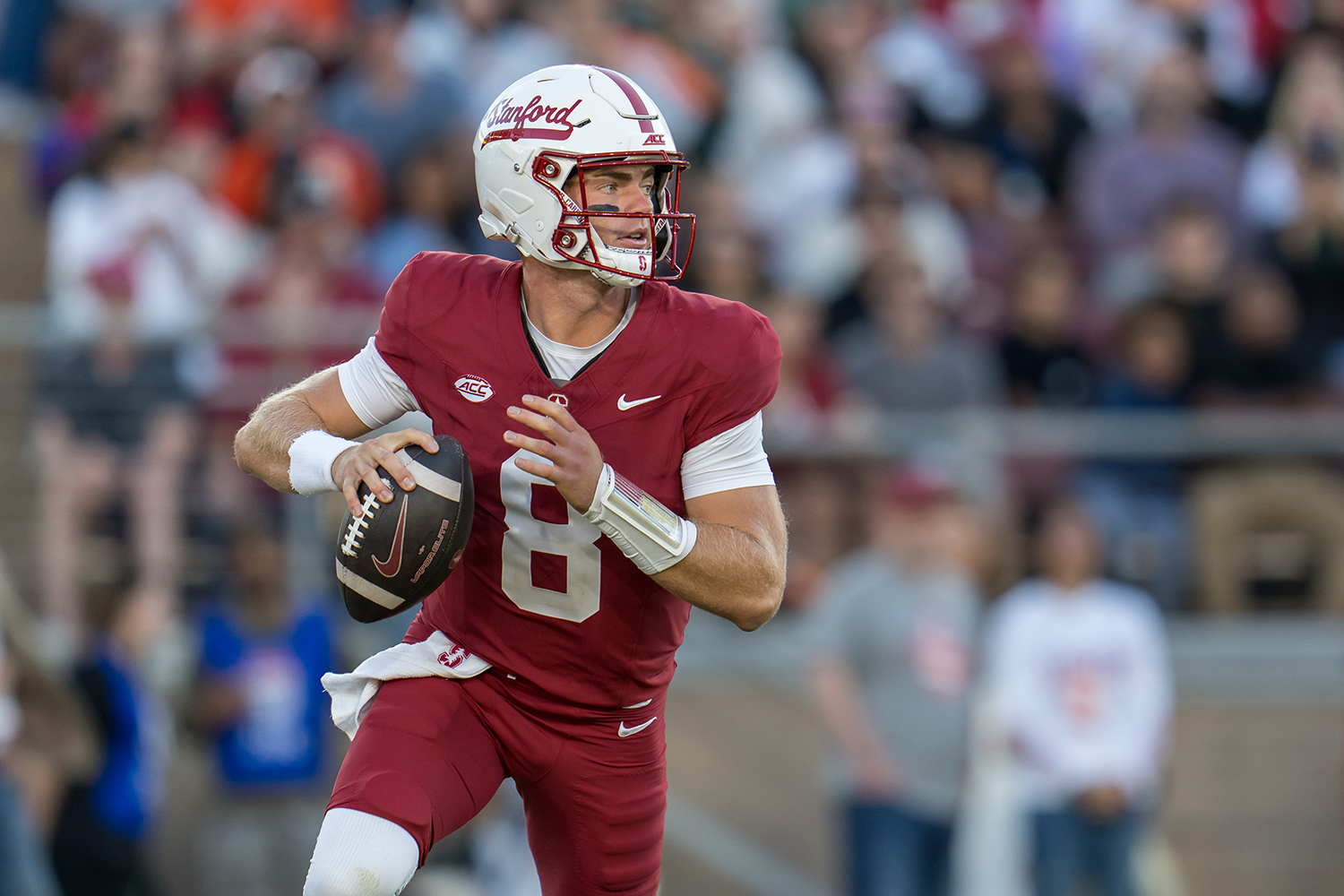 A Cardinal quarterback rolls out with the football in hand as fans blur behind him.