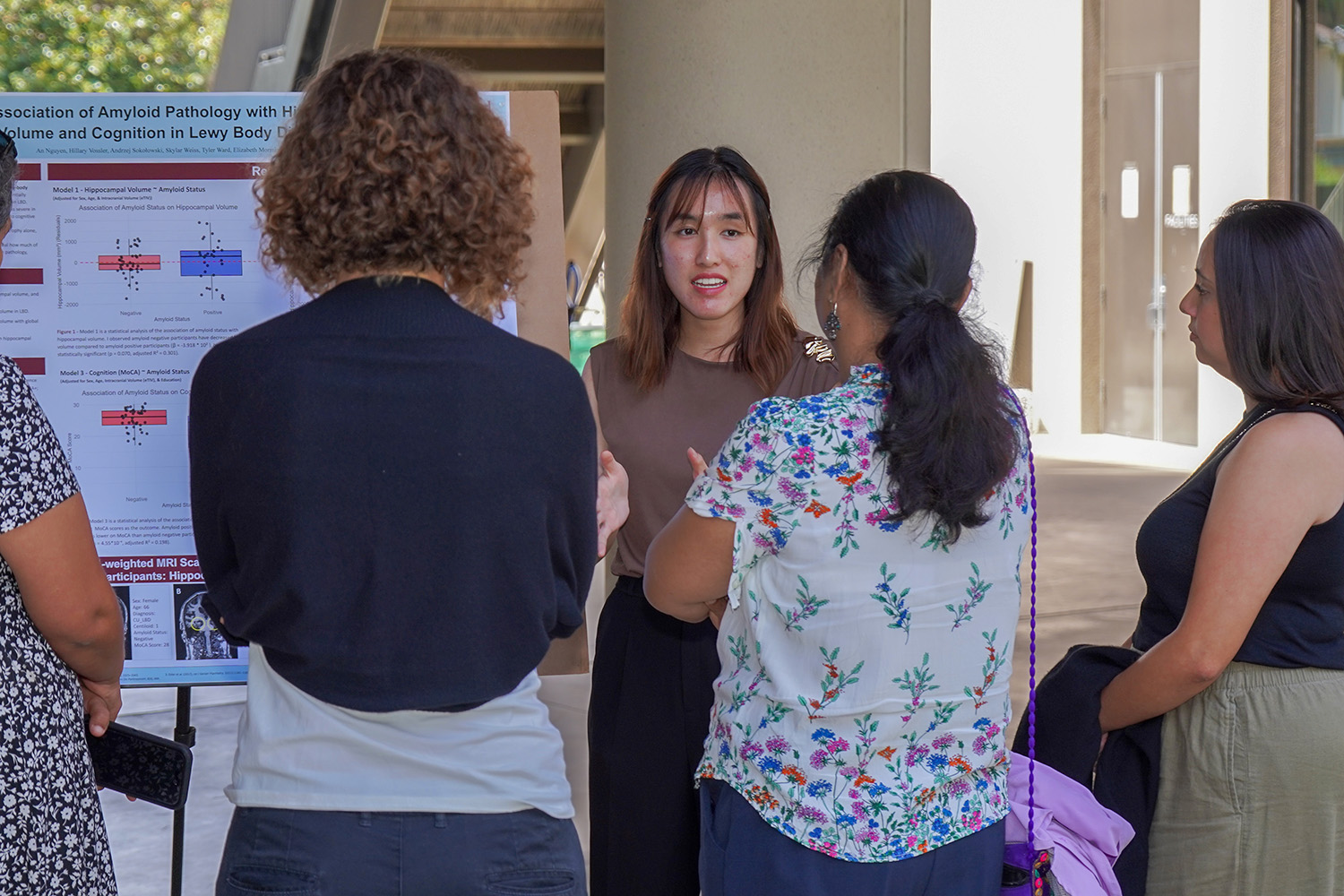 Student presents a scientific poster on brain imaging and memory to a small group at an outdoor conference session.