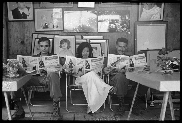 Two soldiers and a young woman reading Overseas Weekly)