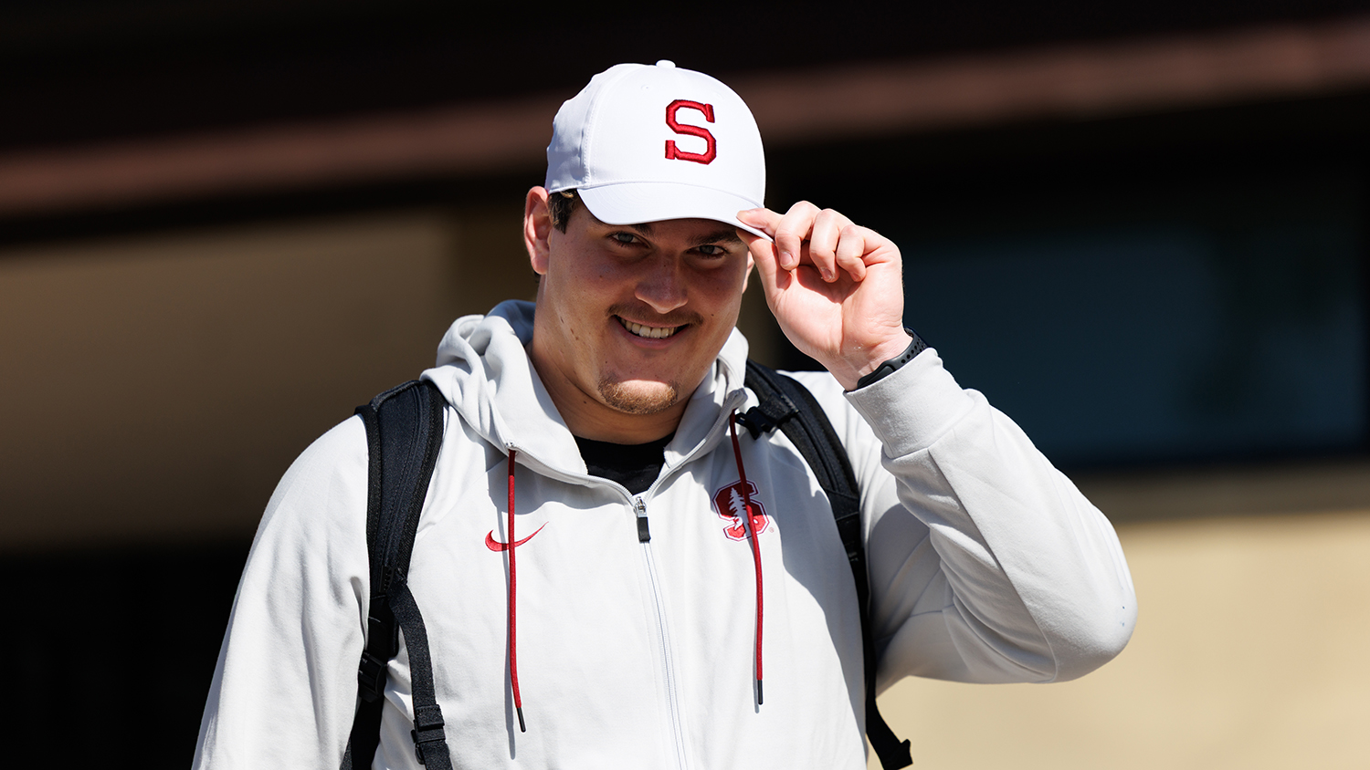 Football offensive lineman Fisher Anderson in white jacket tips his white cap with red Stanford block S logo.