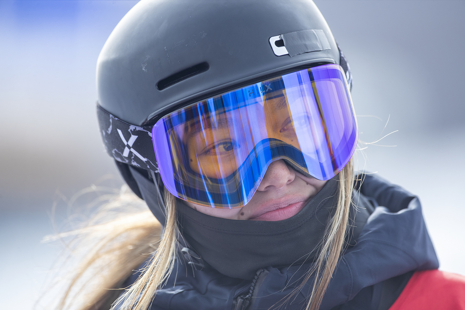 Zoe Atkin in a helmet, goggles, and red jacket on a snowy day.