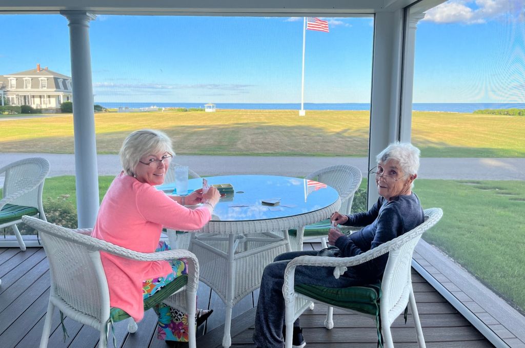 Alice and Gayle Whittemore sit at a table on a porch, enjoying a view of the ocean.