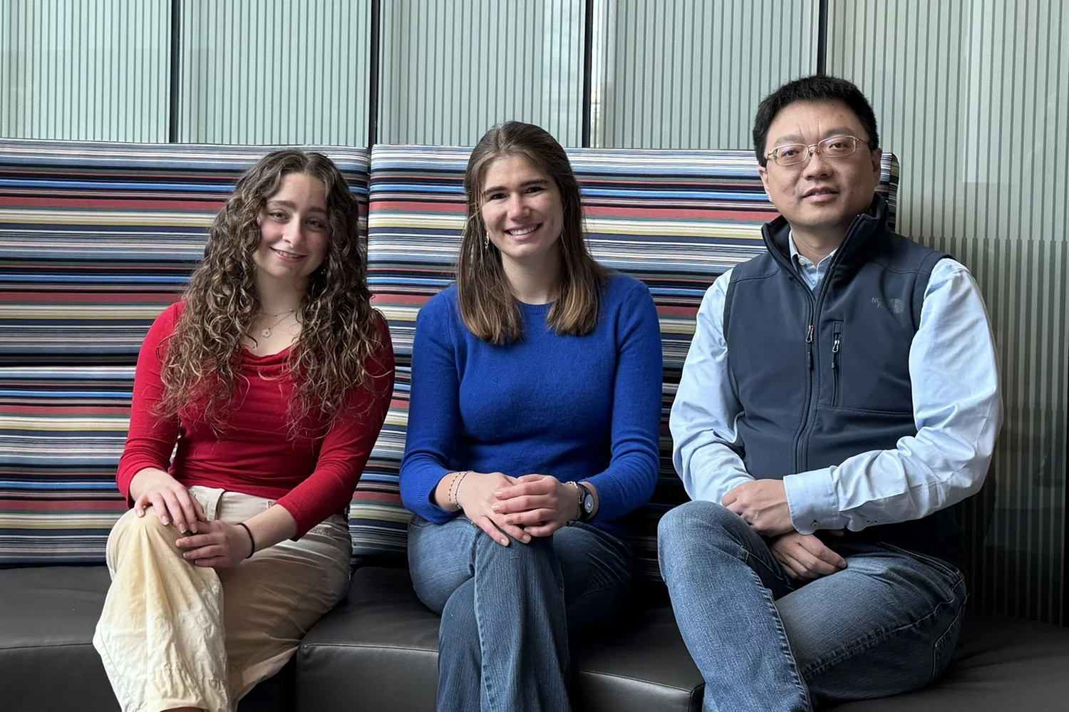 Alice Finkelstein, Heloise Hoffmann, and Stanley Qi sit on a striped couch, dressed casually in colorful attire.