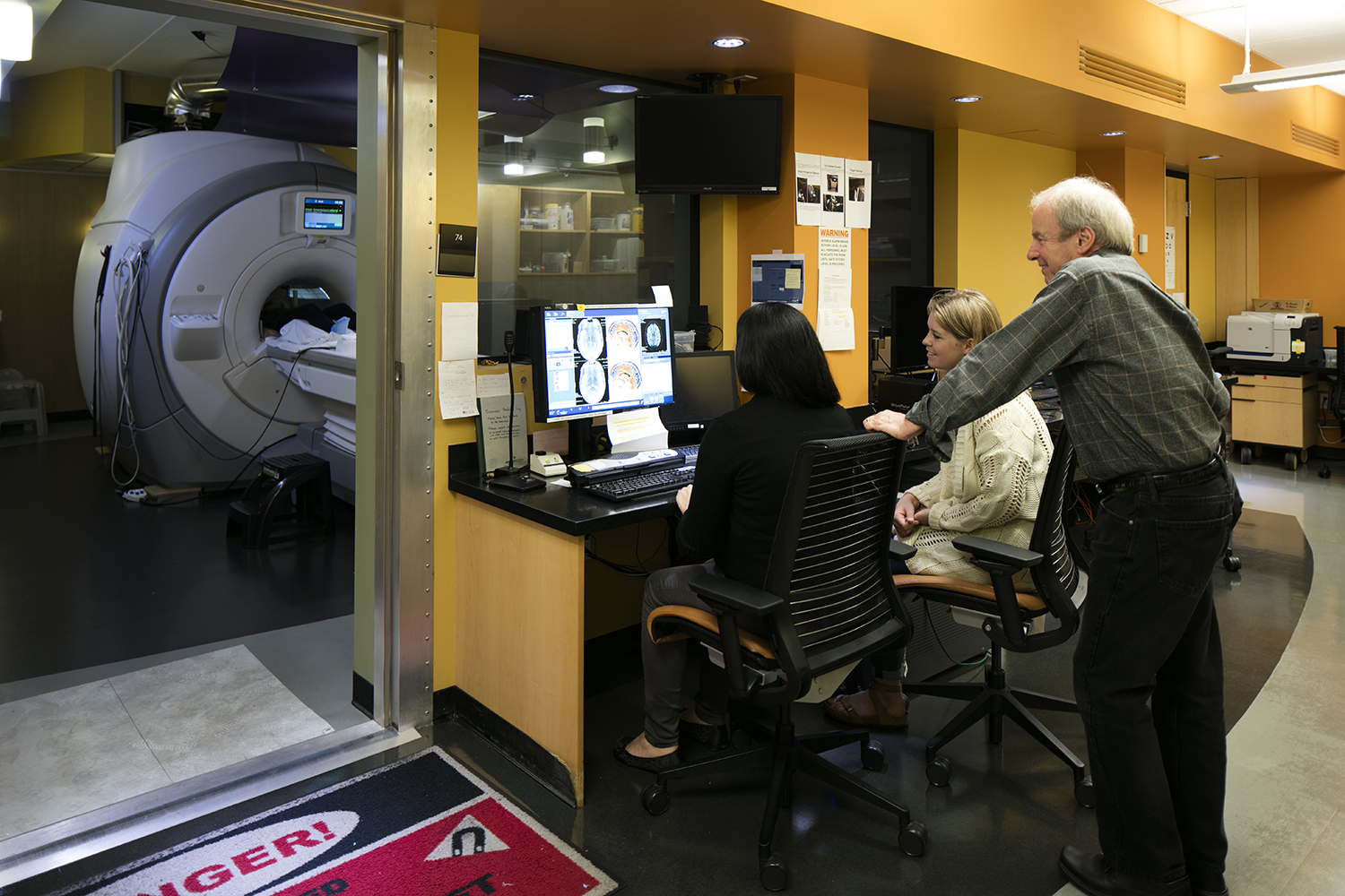 Ian Gotleib and staff members review scan images on a computer while a patient is positioned for an MRI in a clinical setting.