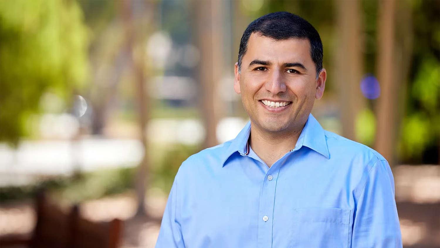 Mohsen Bayati in a light blue shirt stands outdoors against a blurred green background, smiling and posing for the photo.