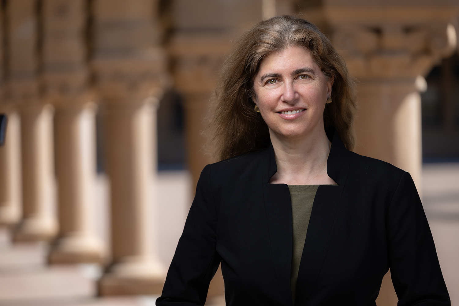 Jessica Riskin in black blazer smiling in the Stanford Quad arcade.