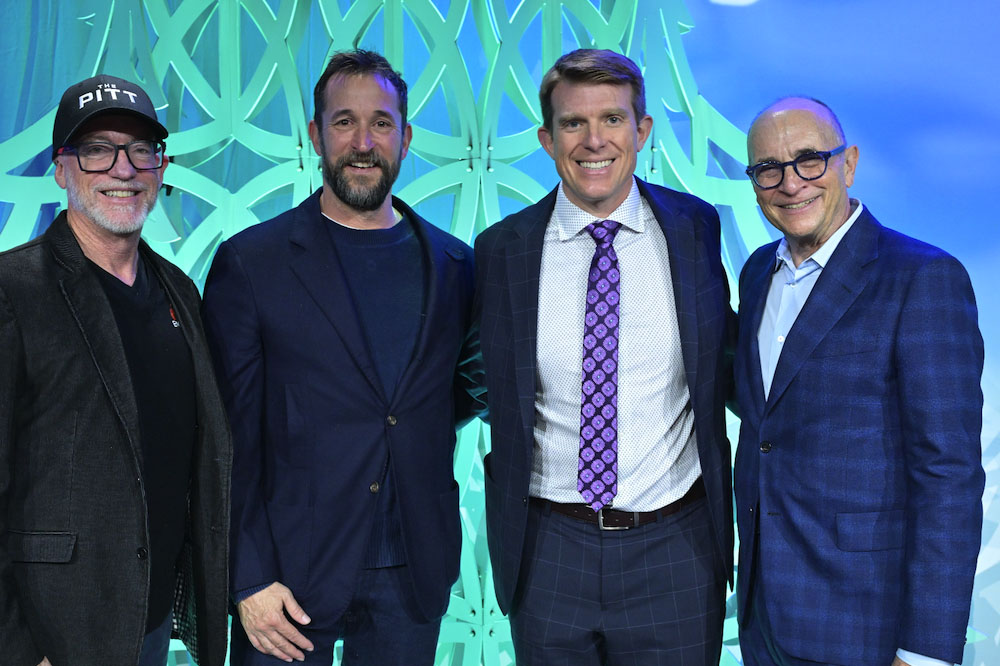 Four men associated with The Pitt pose together at an event, smiling in front of a decorative backdrop.