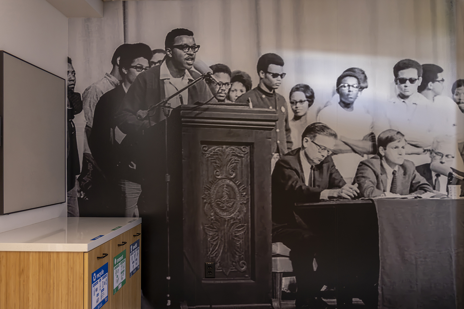 Wall-size image of historic photo of Black Student Union co-chair at lectern taking the mic from Provost Richard Lyman in 1968.