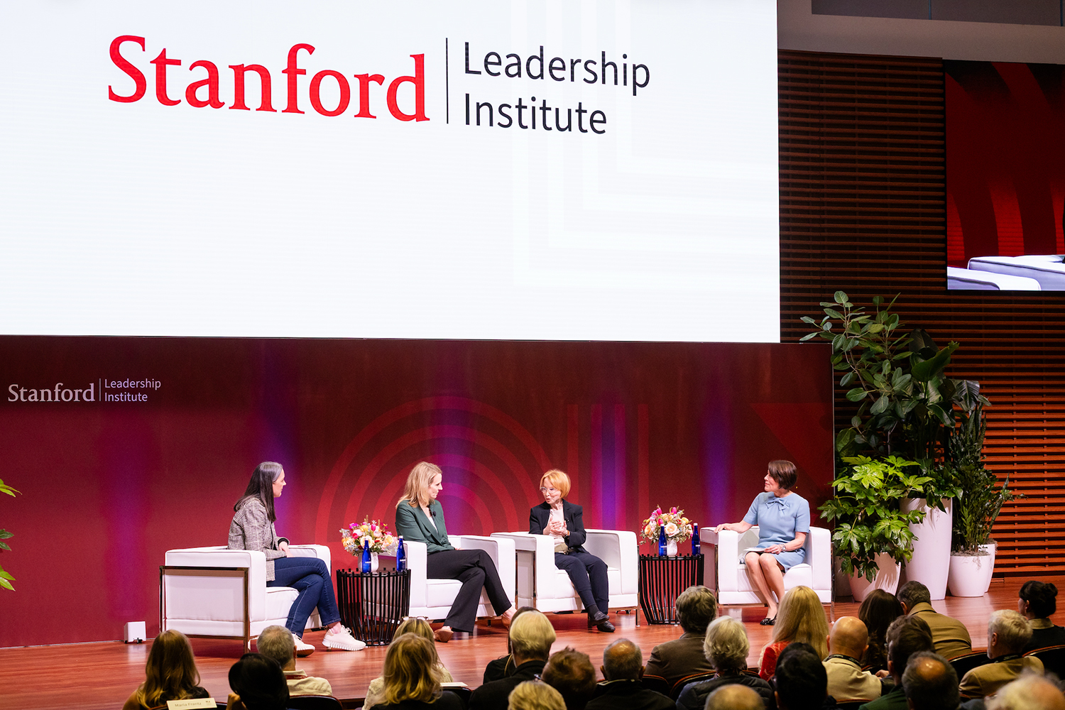 A panel discussion at Stanford Leadership Institute features four speakers seated with an audience, discussing leadership topics on stage.