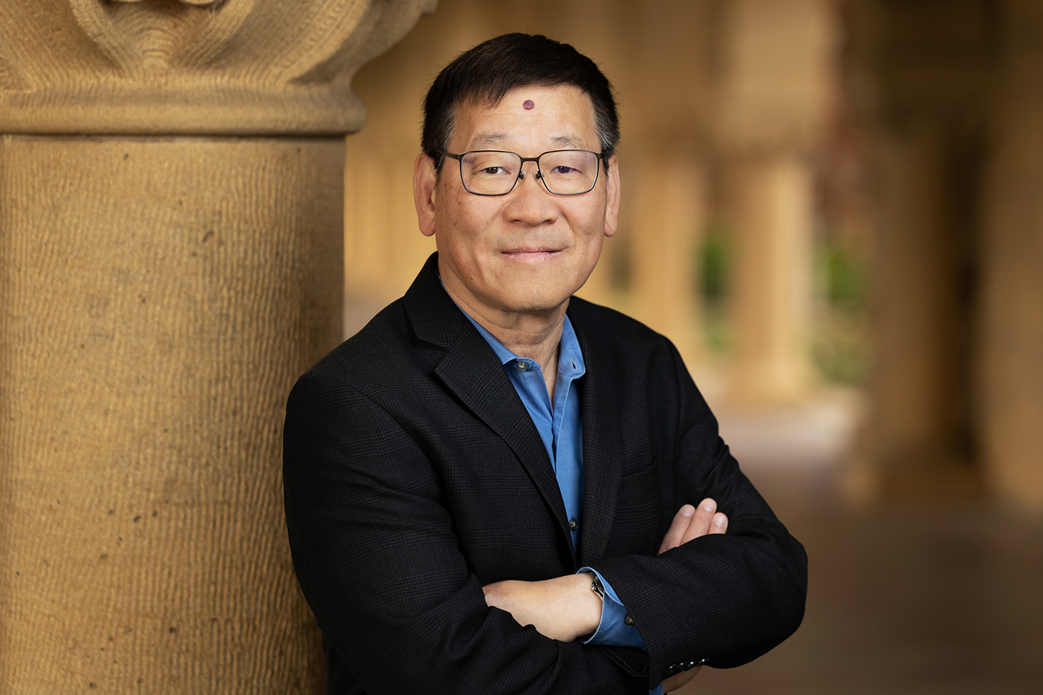 Zhi-Xun Shen poses for a profile photo while leaning against a sandstone column with his arms folded.