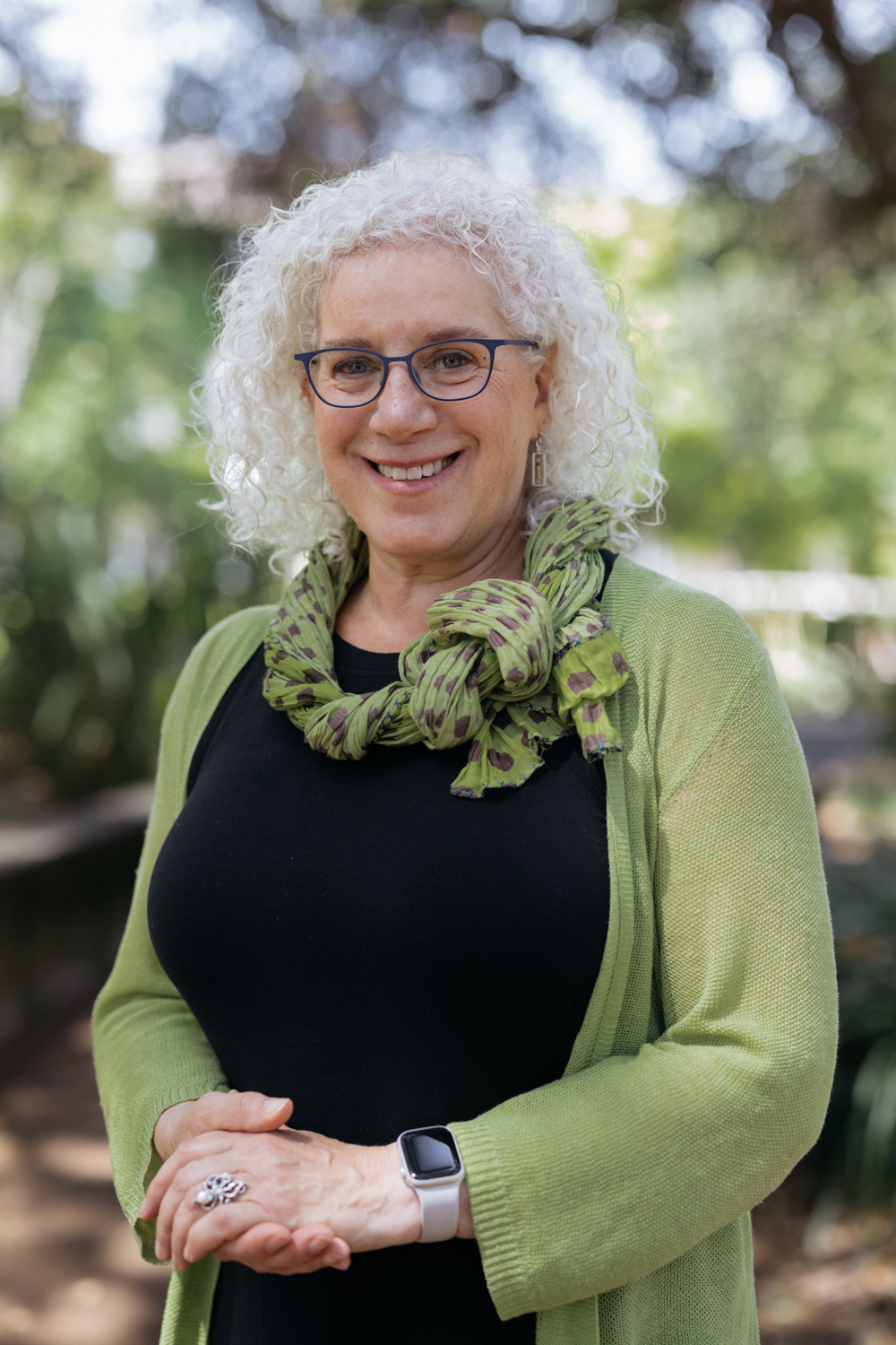 Kleppner with white curly hair and glasses wearing a green cardigan and patterned scarf outdoors.