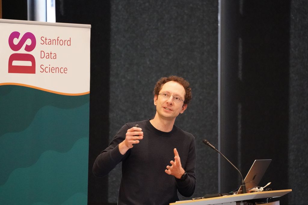 Ludwig Schmidt gestures while speaking at a Stanford Data Science event, with a branded banner in the background.