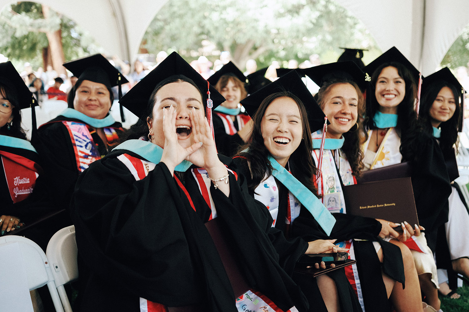 Graduates in caps and gowns sit together during a ceremony, celebrating their academic achievements.