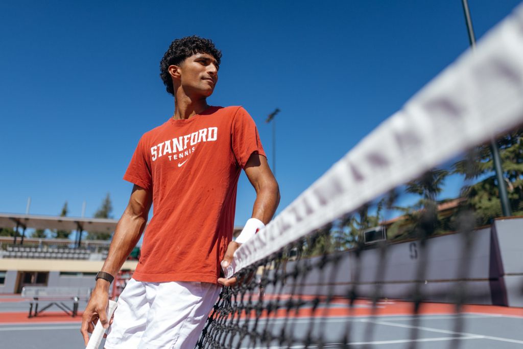 Open video Samir Banerjee wearing a Stanford tennis T-shirt and leaning against a net on an outdoor tennis court. in a modal