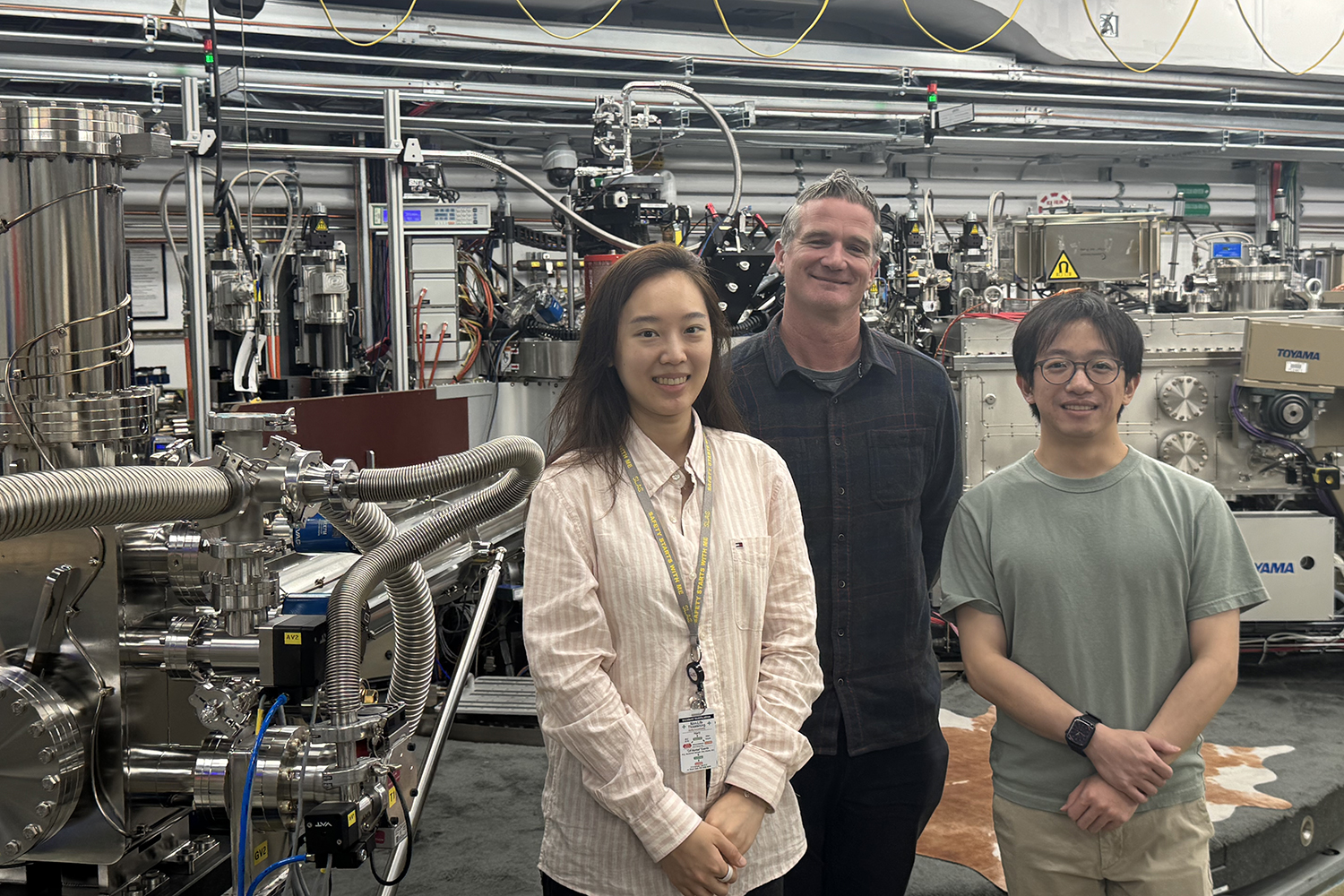 Three researchers stand smiling in front of a large beamline instrument at SLAC.