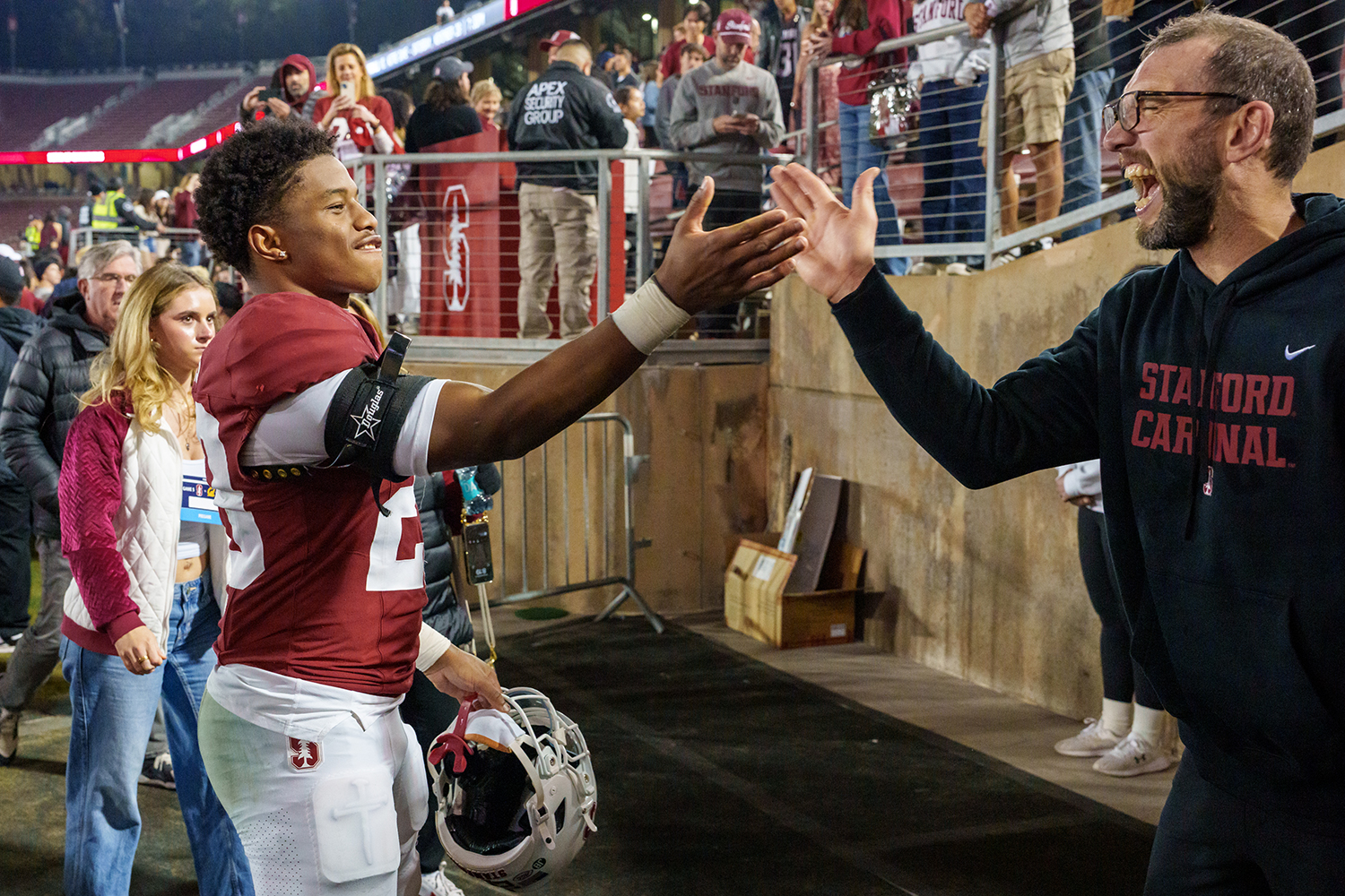A Stanford player and a coach high-five near the stadium tunnel as fans watch from behind a railing.