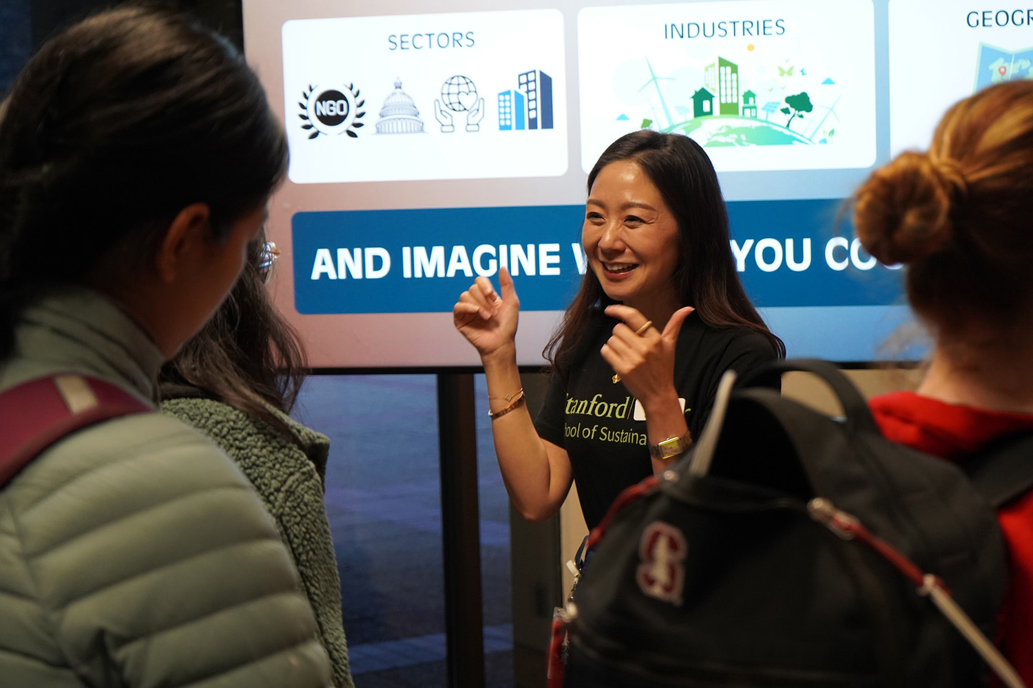 Joyce Lee in a Stanford Sustainability shirt gestures while talking with students near a presentation screen.