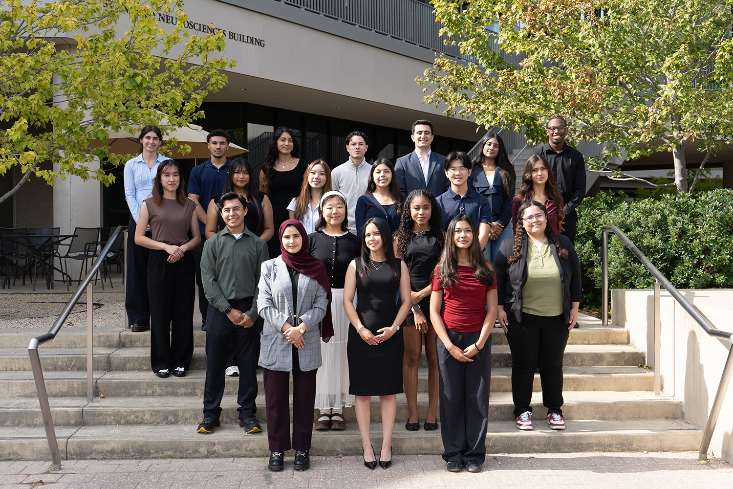 Large group of students poses together on outdoor steps in front of the Neurosciences Building.