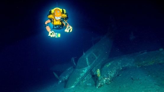 An underwater image of a robot swimming above a submerged airplane