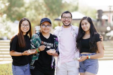 Four friends standing arm-in-arm, one wearing a Stanford t-shirt.