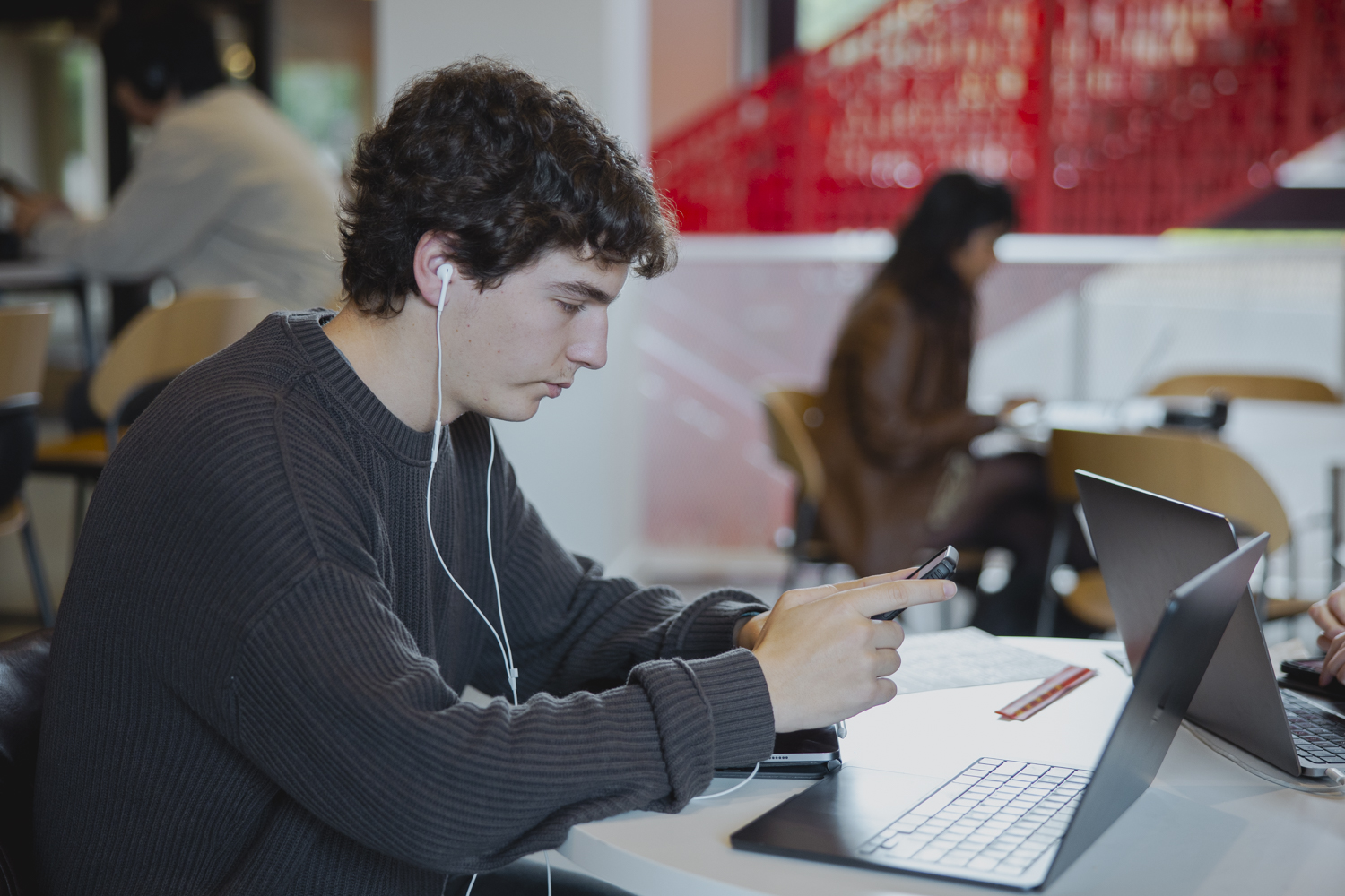 Male student at table on his phone with laptop open in front of him.