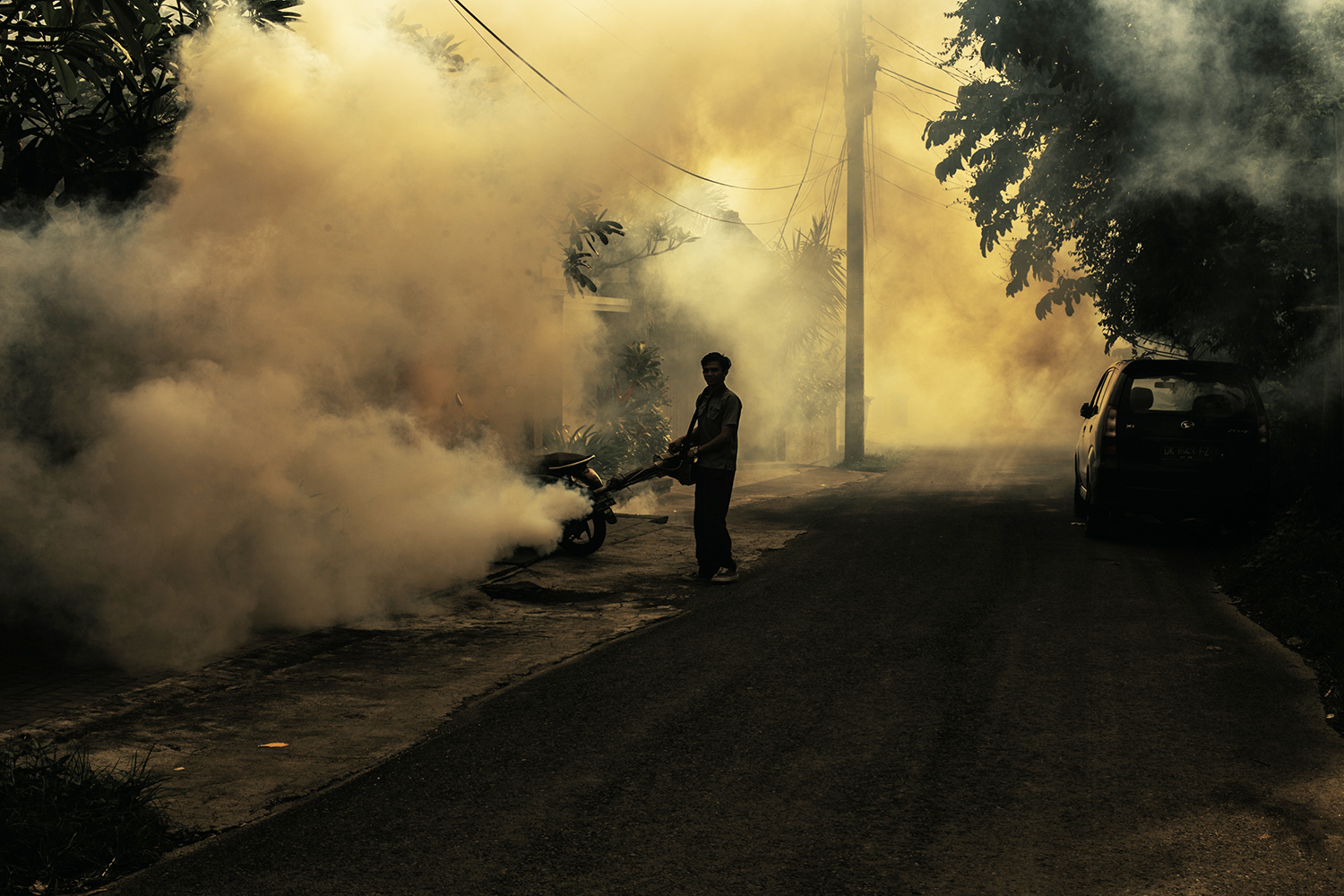 A man in silhouette doing anti-mosquito fogging in a town in Bali, Indonesia.