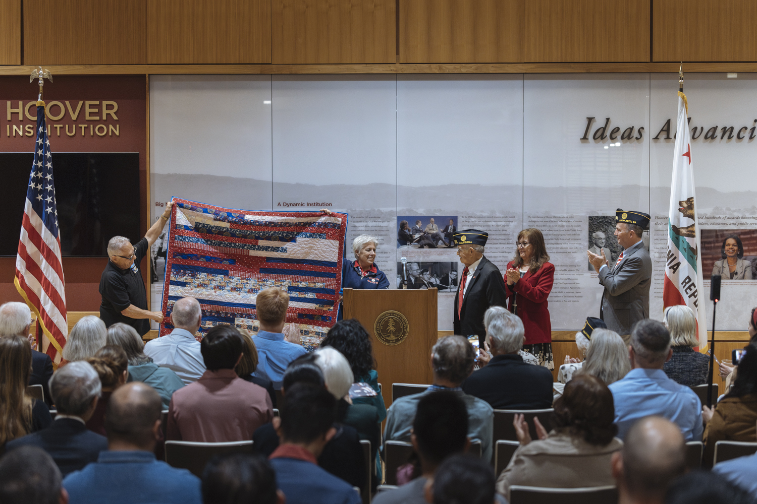 The red, white, and blue quilt of valor is held up for display to the audience before it is presented to U.S. Marine Corps veteran Manny Velasco.