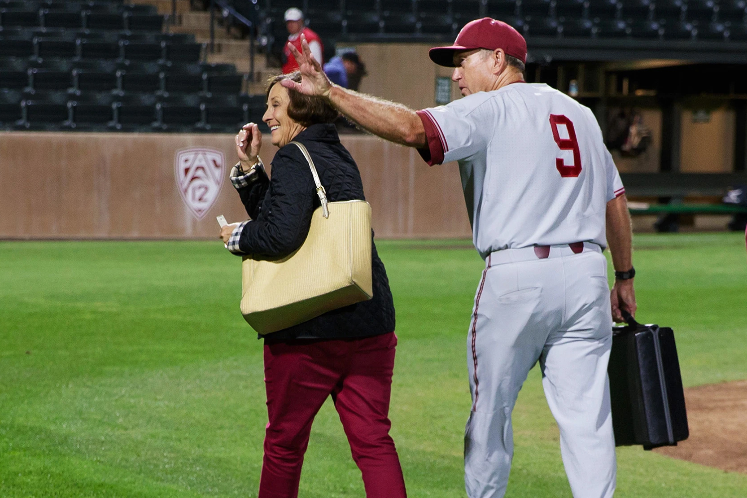 Baseball coach Mark Marquess carrying briefcase waves goodbye while his wife, Susan, carrying a handbag, walk off from the field at night.