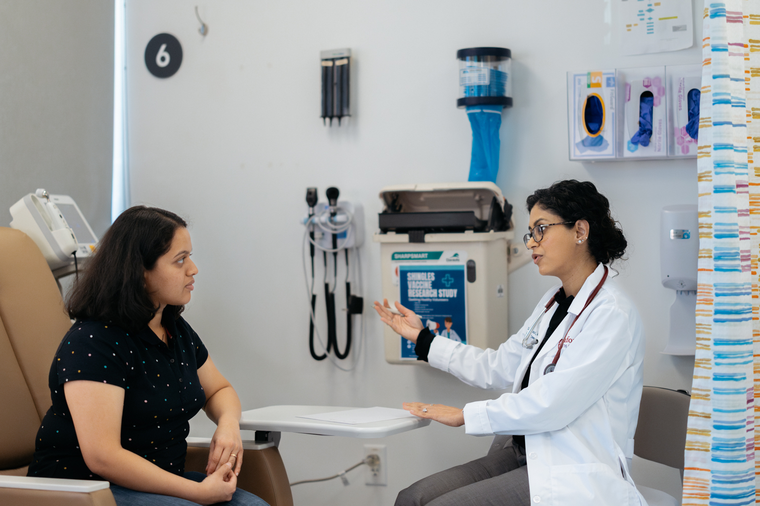 Tina Sindher engages with a patient in a clinical setting, discussing health matters.