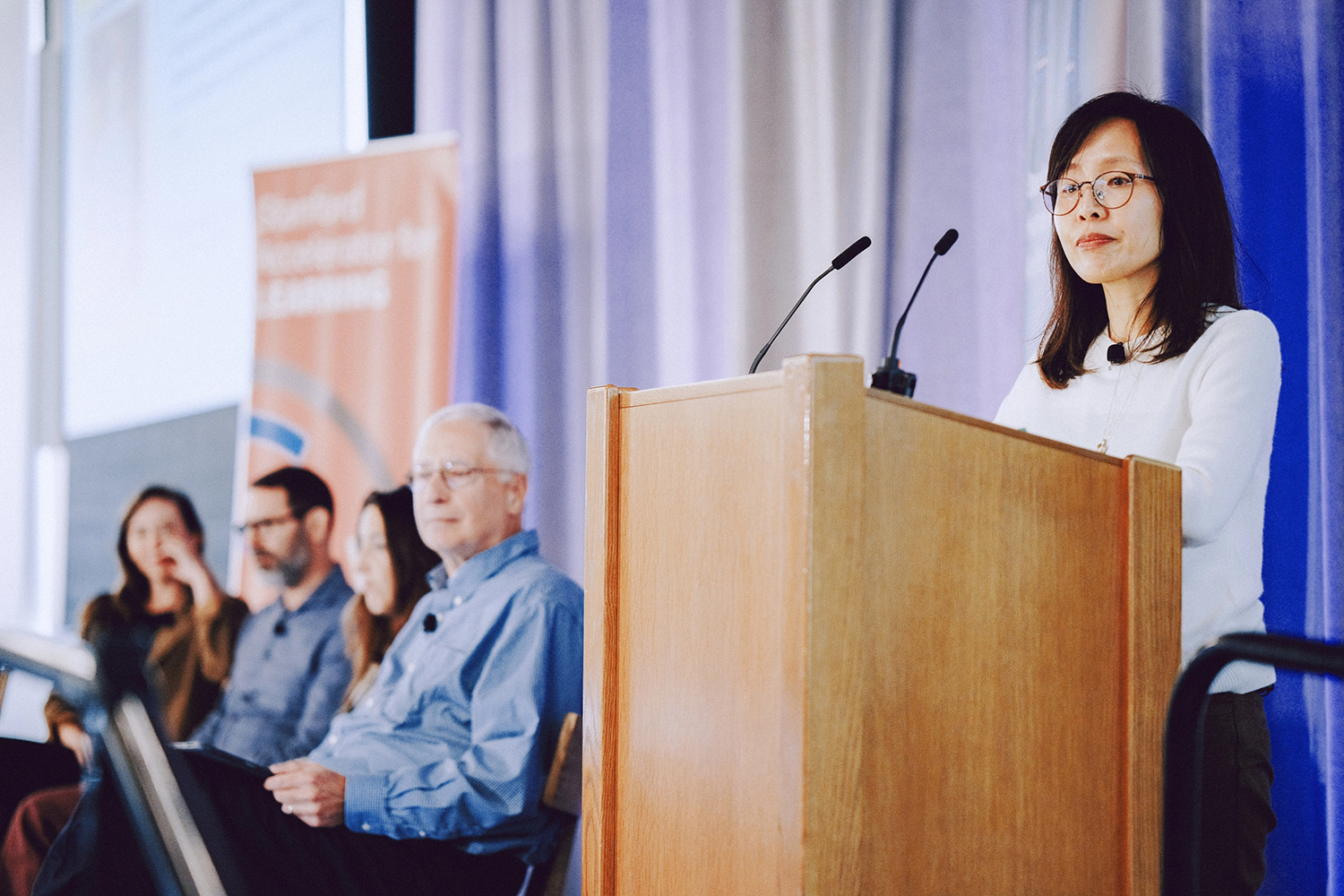 Pilyoung Kim speaks at a podium during a panel discussion, with audience members seated nearby.