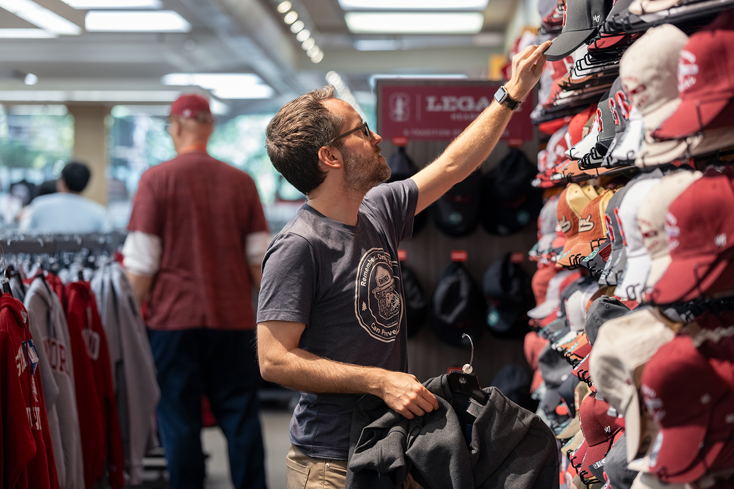 A man examines baseball caps on display while holding a jacket, shopping for Cardinal merch.