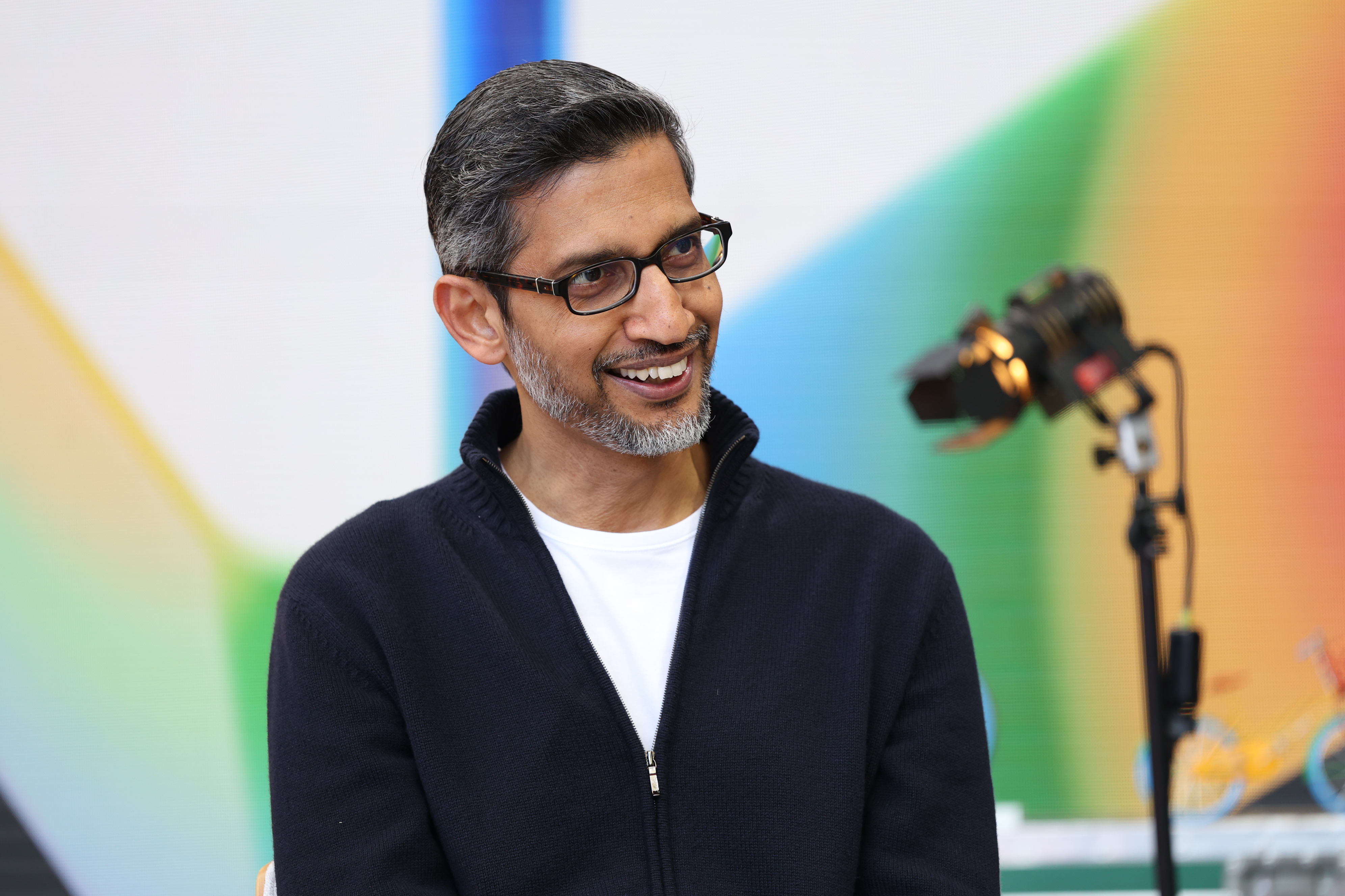 Sundar Pichai smiling in front of a brightly colored background