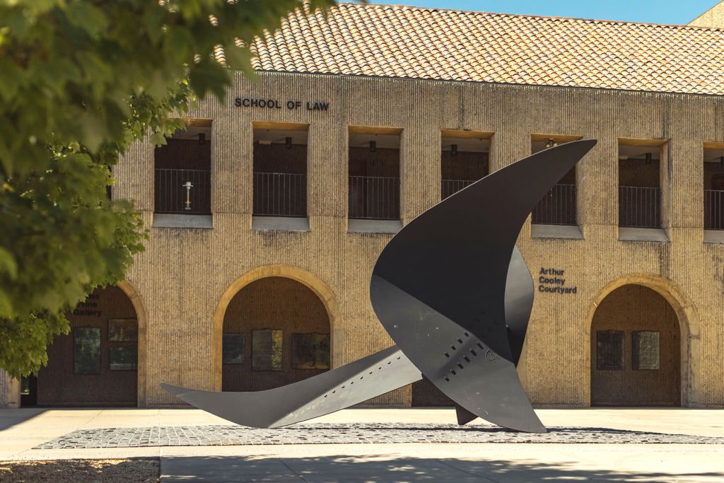 A large, abstract black sculpture stands in front of the School of Law, featuring a textured wall and courtyard.